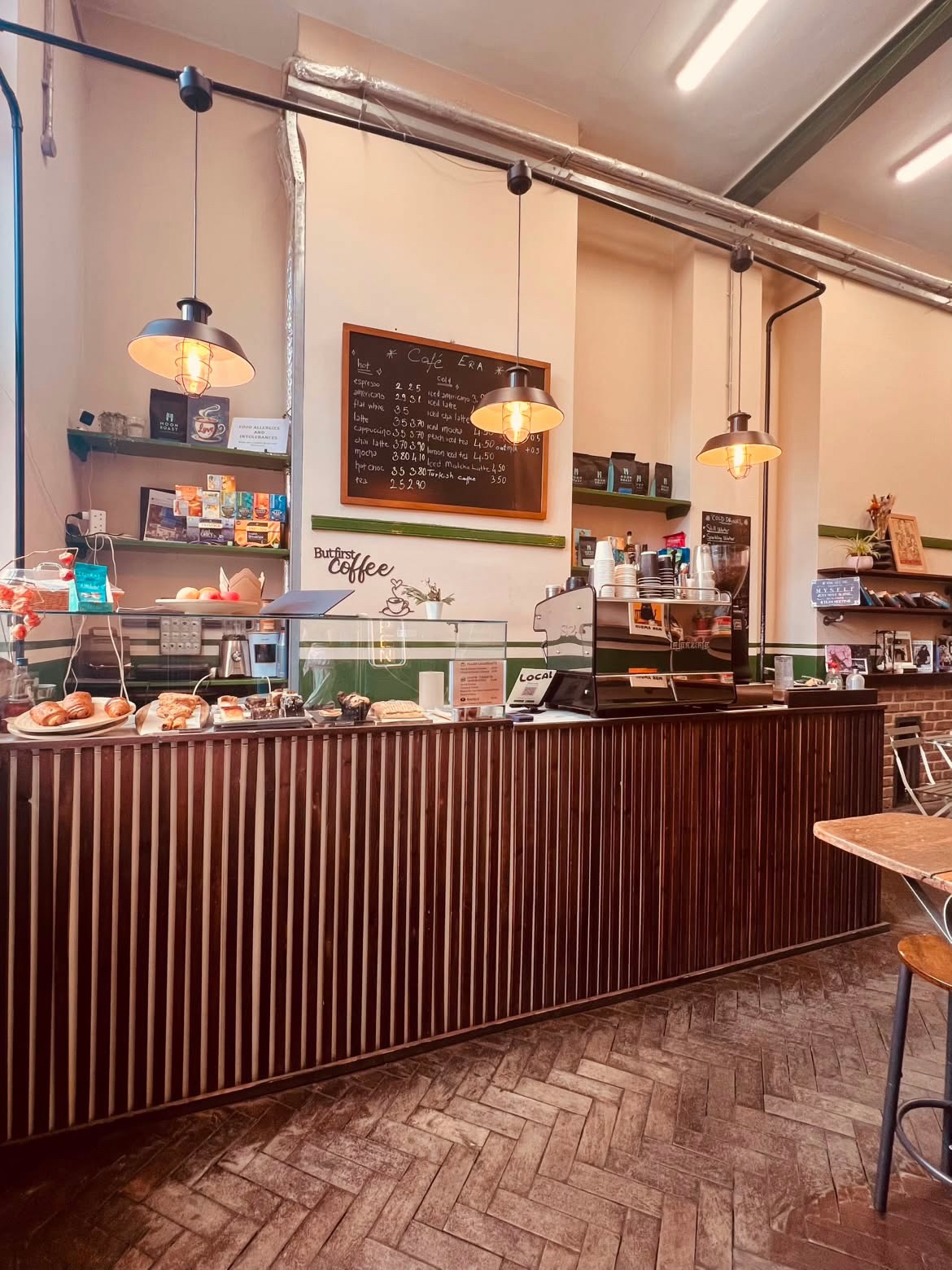 Cafe Era’s wooden coffee counter with fresh pastries and warm pendant lighting inside Queenstown Road Station